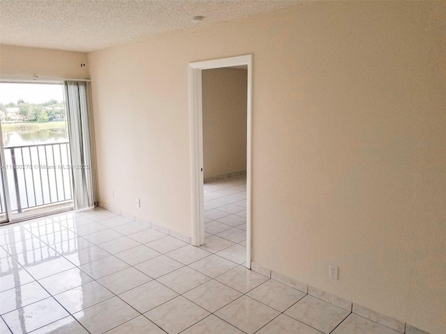 empty room featuring light tile patterned flooring, a water view, and a textured ceiling