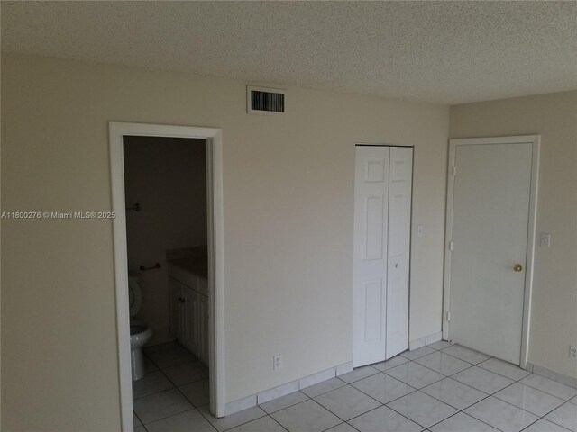 unfurnished bedroom with light tile patterned floors, a textured ceiling, a closet, and ensuite bathroom