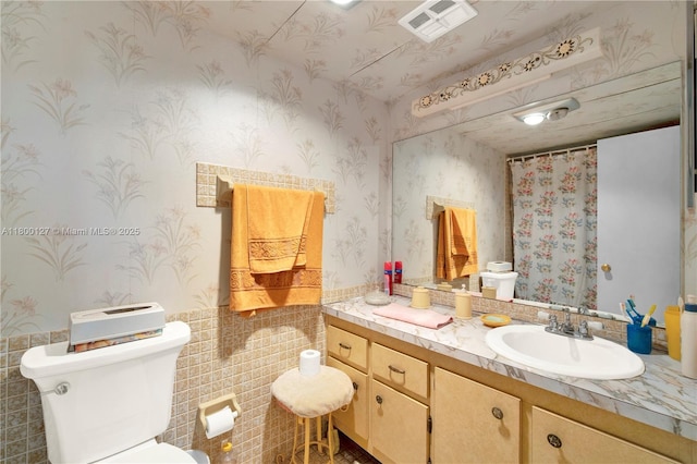 full bathroom featuring wallpapered walls, a wainscoted wall, toilet, vanity, and tile walls
