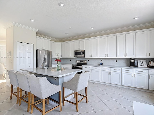 16435 SW 27th St, Miramar, FL 33027 - kitchen with appliances with stainless steel finishes, ornamental molding, light tile patterned flooring, white cabinetry, and a kitchen breakfast bar