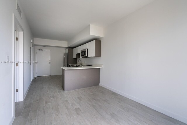 321 NE 26th St Unit 614, Miami, FL 33137 - kitchen with appliances with stainless steel finishes, light wood-style floors, light countertops, a peninsula, and white cabinets
