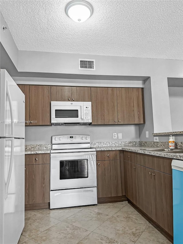 kitchen featuring white appliances, a textured ceiling, a sink, light countertops, and light tile patterned flooring