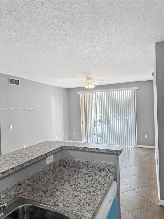 kitchen featuring dishwashing machine, ceiling fan, a textured ceiling, light tile patterned flooring, and light countertops