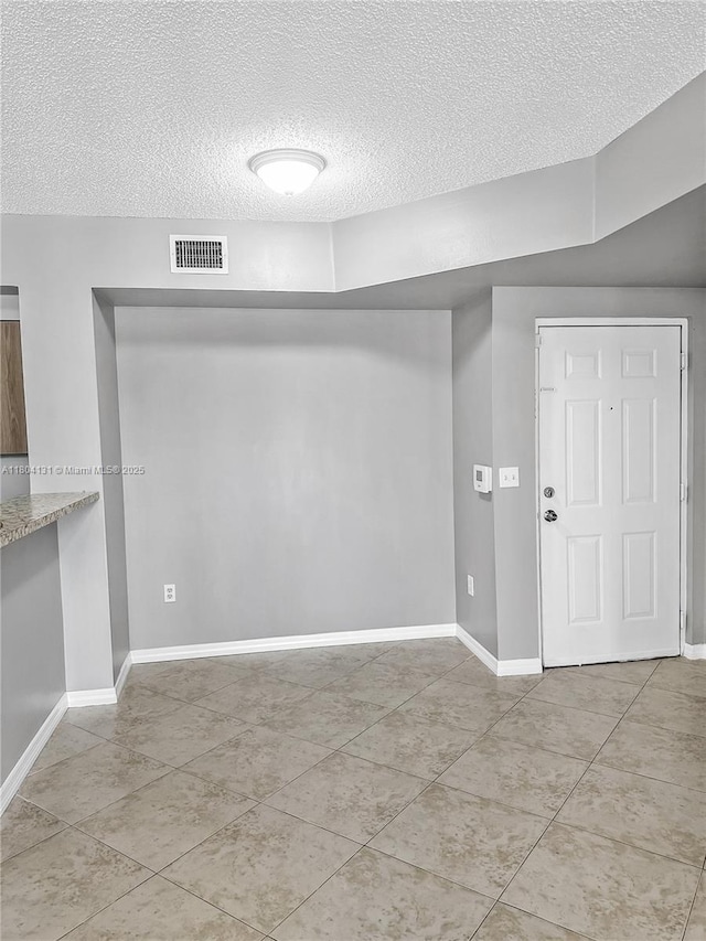 tiled spare room with a textured ceiling and baseboards