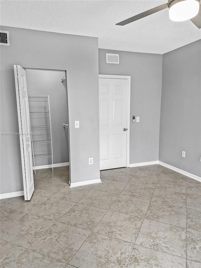 unfurnished bedroom with a textured ceiling, a walk in closet, tile patterned flooring, ceiling fan, and baseboards