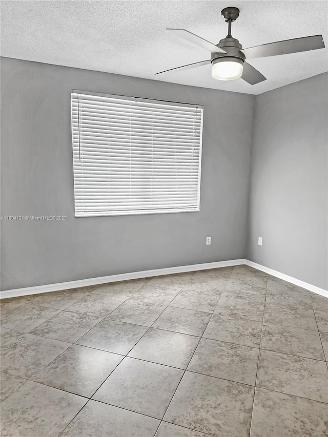 spare room with a textured ceiling, ceiling fan, tile patterned floors, and baseboards