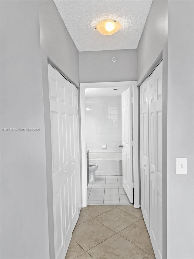 hall featuring light tile patterned floors and a textured ceiling