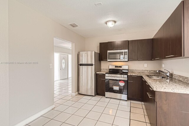3226 NW 41st St, Lauderdale Lakes, FL 33309 - kitchen with appliances with stainless steel finishes, a sink, dark brown cabinetry, a textured ceiling, and light stone counters