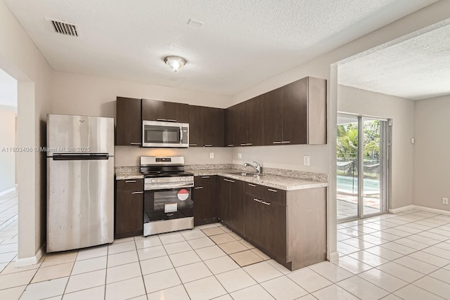 3226 NW 41st St, Lauderdale Lakes, FL 33309 - kitchen with appliances with stainless steel finishes, a textured ceiling, a sink, dark brown cabinetry, and light tile patterned flooring