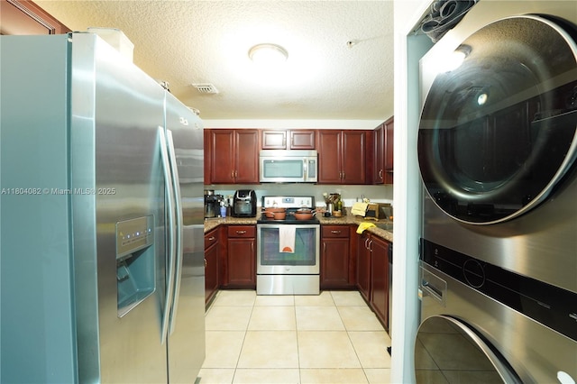 5271 SW 8th St Unit 311, Miami, FL 33134 - kitchen with stainless steel appliances, reddish brown cabinets, stacked washing machine and dryer, light tile patterned floors, and a textured ceiling
