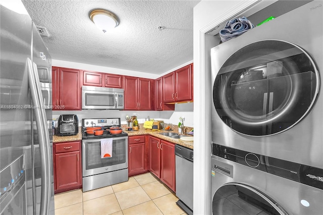 5271 SW 8th St Unit 311, Miami, FL 33134 - kitchen with appliances with stainless steel finishes, stacked washing machine and dryer, reddish brown cabinets, a sink, and light tile patterned flooring
