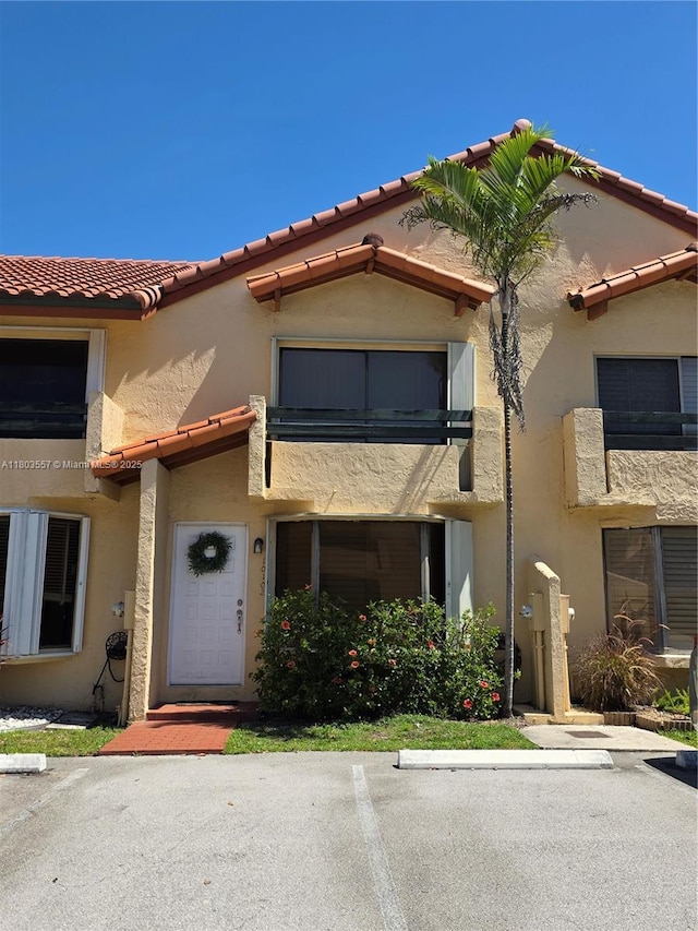 view of front facade featuring stucco siding, a tiled roof, uncovered parking, and a balcony