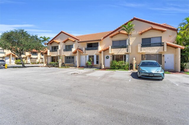 view of property featuring stucco siding, uncovered parking, and a tiled roof