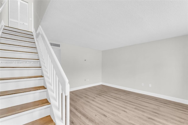 stairs featuring wood finished floors, a textured ceiling, and baseboards