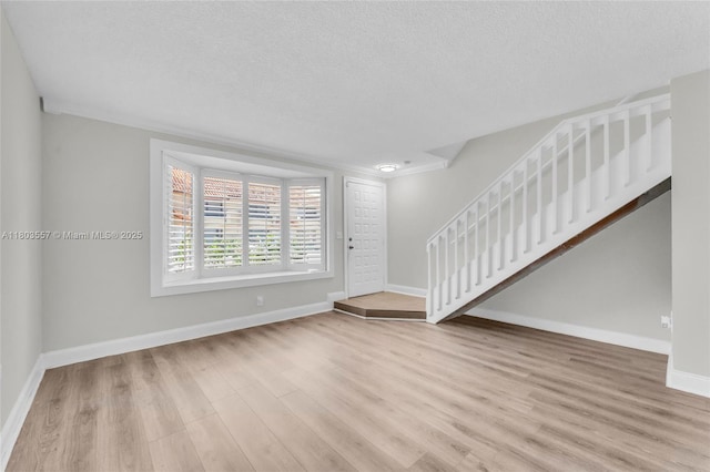 entrance foyer featuring wood finished floors, baseboards, a textured ceiling, stairs, and crown molding