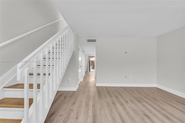 stairway with wood finished floors, a textured ceiling, and baseboards
