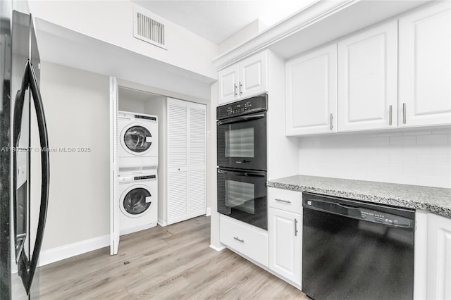 kitchen featuring black appliances, stacked washer and clothes dryer, light wood finished floors, backsplash, and white cabinetry