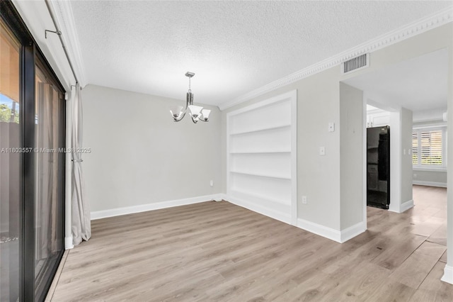 spare room with built in shelves, a textured ceiling, a chandelier, baseboards, and light wood finished floors