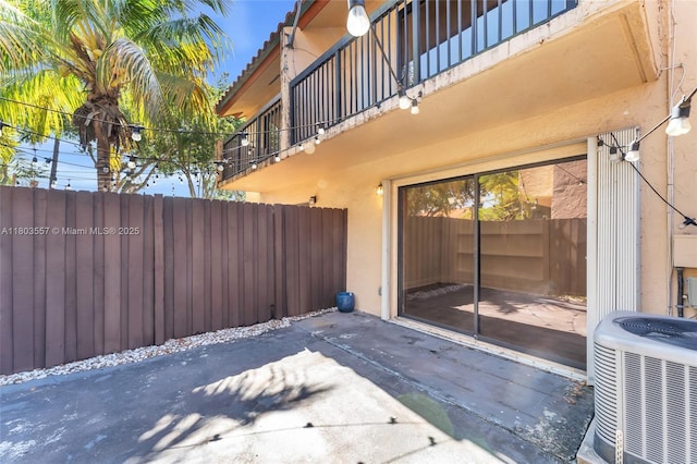 view of patio featuring central AC unit, fence, and a balcony