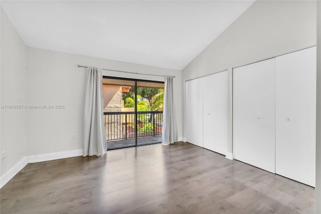 unfurnished bedroom with access to exterior, multiple closets, wood finished floors, high vaulted ceiling, and baseboards