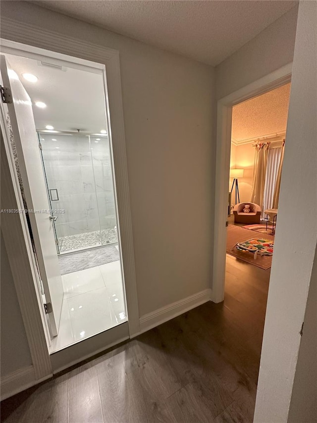 bathroom with a shower stall, wood finished floors, baseboards, and a textured ceiling