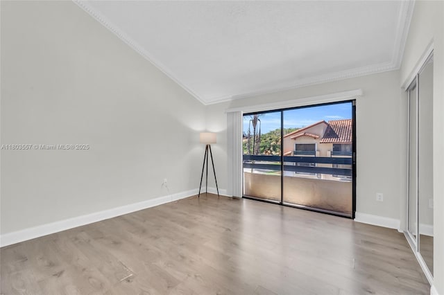 empty room with ornamental molding, wood finished floors, baseboards, and vaulted ceiling