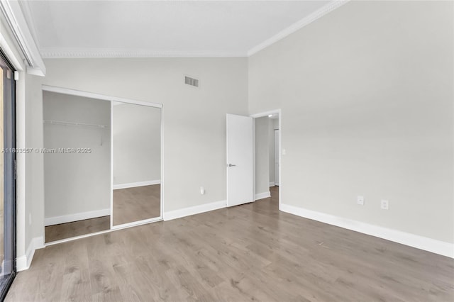 unfurnished bedroom featuring crown molding, wood finished floors, a closet, baseboards, and high vaulted ceiling