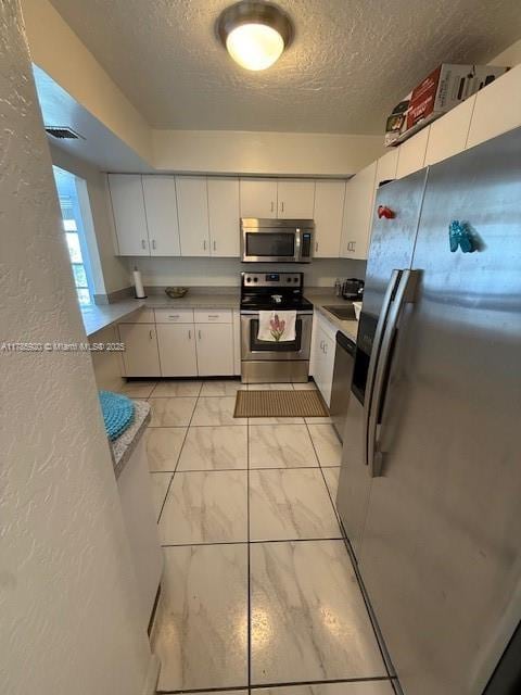 801 Three Islands Blvd Unit 302, Hallandale Beach, FL 33009 - kitchen with appliances with stainless steel finishes, a textured ceiling, white cabinetry, light marble finish floors, and a textured wall