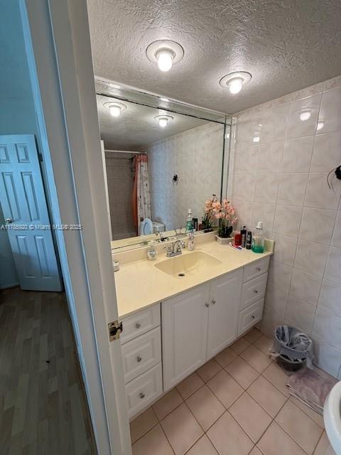 801 Three Islands Blvd Unit 302, Hallandale Beach, FL 33009 - full bath with a textured ceiling, vanity, curtained shower, tile walls, and tile patterned floors