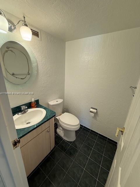 801 Three Islands Blvd Unit 302, Hallandale Beach, FL 33009 - half bath with a textured wall, a textured ceiling, toilet, vanity, and tile patterned flooring