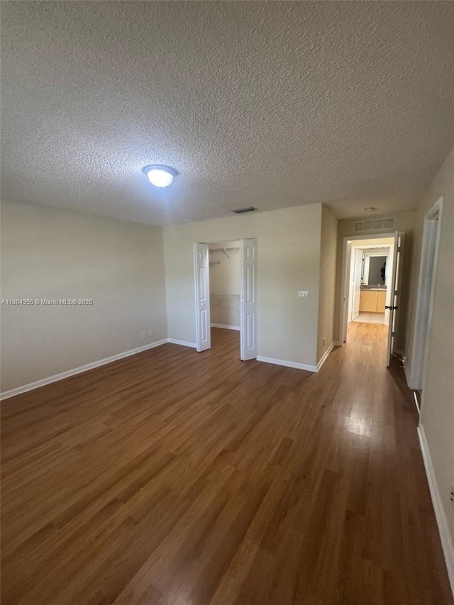 unfurnished room featuring a textured ceiling, dark wood-style flooring, and baseboards