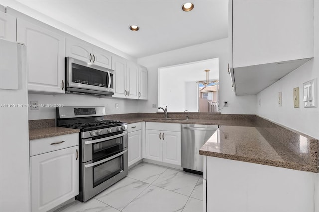 kitchen featuring stainless steel appliances, a sink, recessed lighting, light marble finish floors, and white cabinets