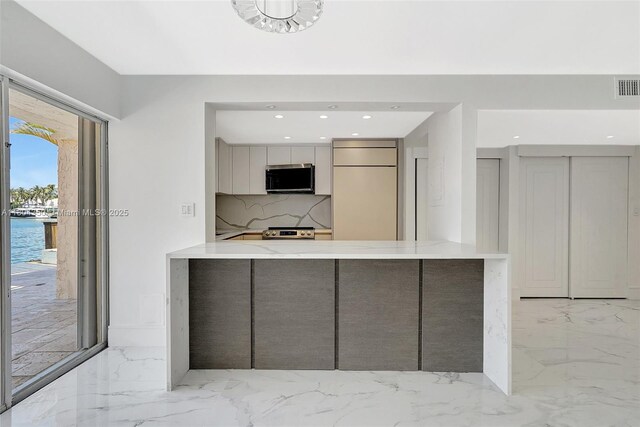 2807 NE 164th St Unit 2, North Miami Beach, FL 33160 - kitchen with appliances with stainless steel finishes, light marble finish floors, modern cabinets, backsplash, and a peninsula