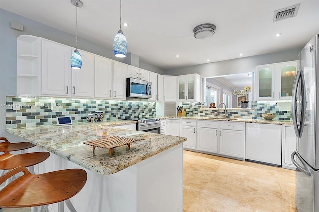 kitchen featuring stainless steel appliances, glass insert cabinets, a sink, tasteful backsplash, and a peninsula