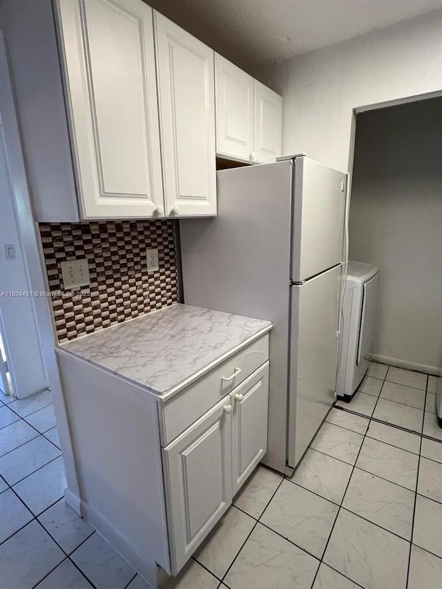 927 NE 199th St Unit 102, Miami, FL 33179 - kitchen featuring washer / clothes dryer, light marble finish flooring, light countertops, white cabinets, and decorative backsplash