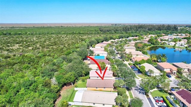 aerial view of property and surrounding area featuring nearby suburban area, a heavily wooded area, and a nearby body of water