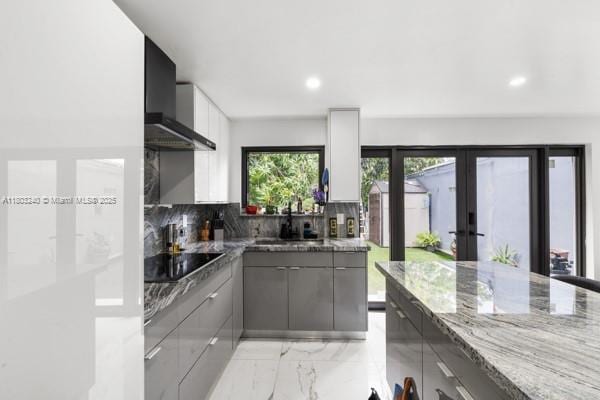 kitchen featuring gray cabinets, black electric cooktop, french doors, light marble finish flooring, and light stone countertops
