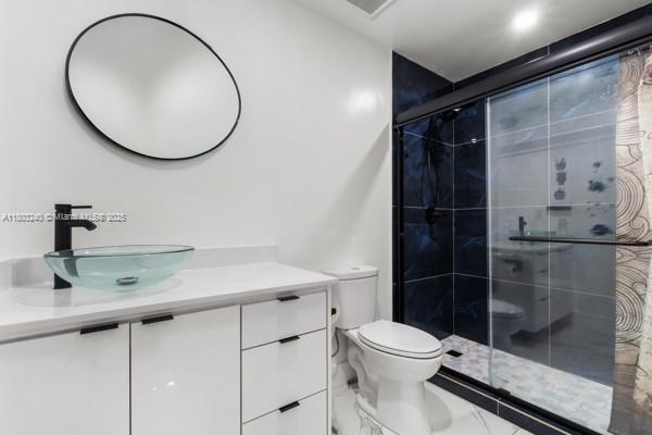 bathroom with a shower stall, vanity, toilet, and marble finish flooring
