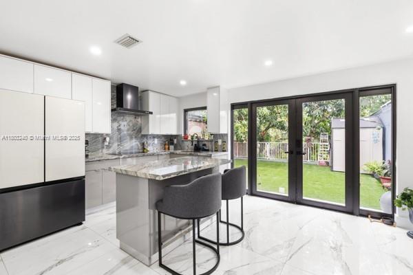 1594 W 73rd St, Hialeah, FL 33014 - kitchen featuring freestanding refrigerator, wall chimney exhaust hood, modern cabinets, light marble finish flooring, and recessed lighting