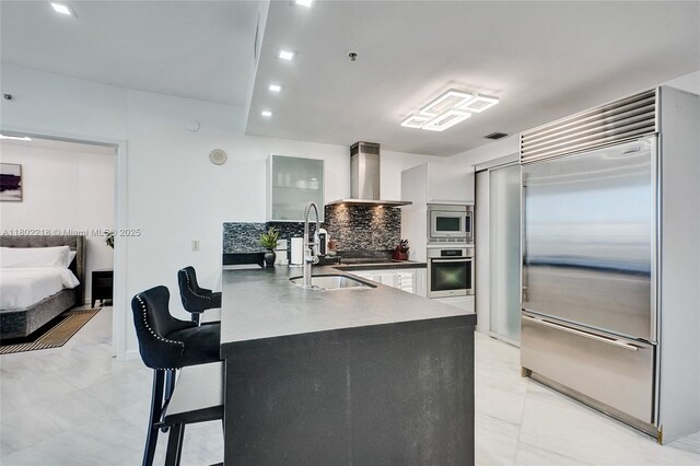 18201 Collins Ave Unit 808, Sunny Isles Beach, FL 33160 - kitchen with built in appliances, wall chimney exhaust hood, dark countertops, a kitchen bar, and a peninsula