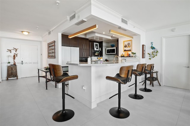 3400 SW 27th Ave Unit 1102, Miami, FL 33133 - kitchen with a kitchen bar, crown molding, light countertops, and dark brown cabinetry