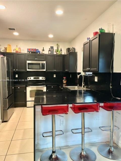 380 NE 37th Ter, Homestead, FL 33033 - kitchen featuring stainless steel appliances, a sink, dark countertops, a peninsula, and a kitchen breakfast bar