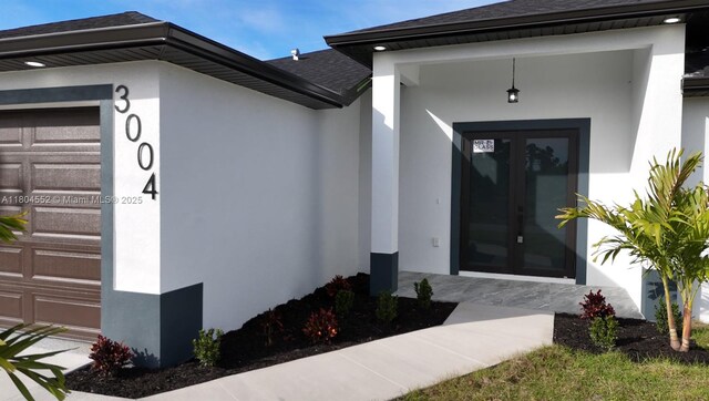 3004 SW 4th St, Lehigh Acres, FL 33976 - doorway to property featuring stucco siding, a shingled roof, french doors, and an attached garage