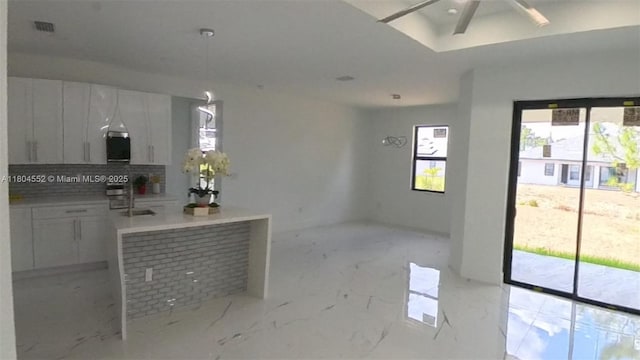 3004 SW 4th St, Lehigh Acres, FL 33976 - kitchen featuring white cabinetry, decorative backsplash, light marble finish floors, a ceiling fan, and hanging light fixtures