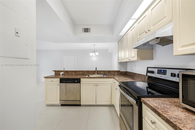 kitchen with stainless steel appliances, under cabinet range hood, a sink, a tray ceiling, and a chandelier
