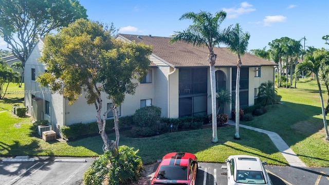view of front of home featuring stucco siding, uncovered parking, a front lawn, and central AC