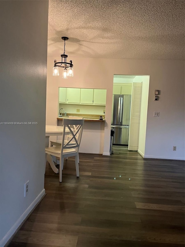 unfurnished dining area featuring a textured ceiling, dark wood-style floors, a chandelier, and baseboards