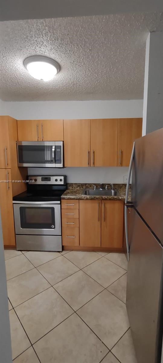 kitchen with appliances with stainless steel finishes, a sink, a textured ceiling, and light tile patterned floors
