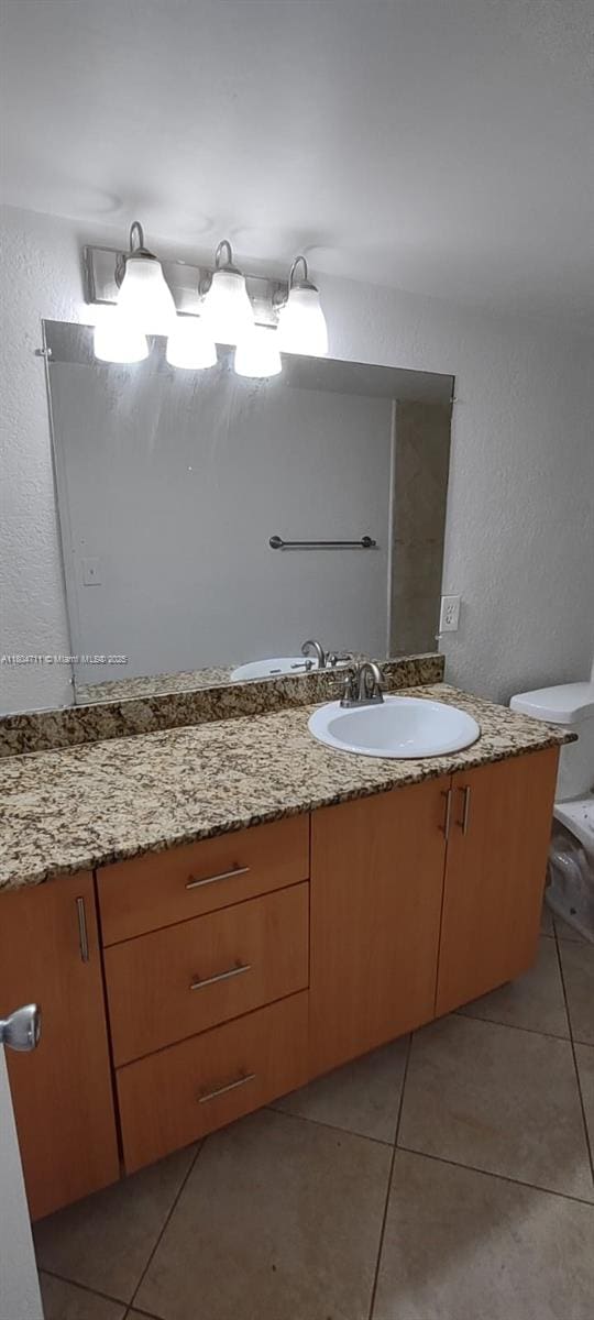 bathroom with tile patterned floors, vanity, toilet, and a textured wall