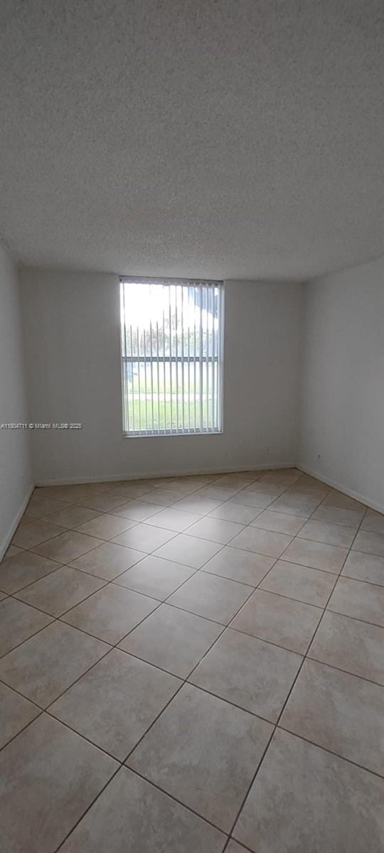 unfurnished room featuring light tile patterned flooring, a textured ceiling, and baseboards